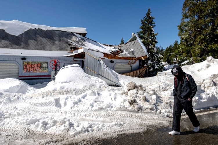 A man walks past a damaged tire shop in Crestline, Calif., Friday, March 3, 2023, following a huge snowfall that buried homes and businesses.