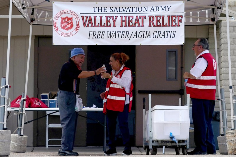 A Salvation Army volunteer hands a bottle of water to a man at a heat relief station as one of her colleagues looks on.
