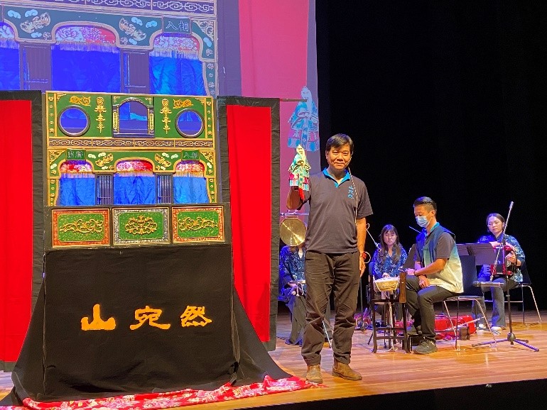A person standing on a stage with a group of people playing instruments

Description automatically generated with low confidence